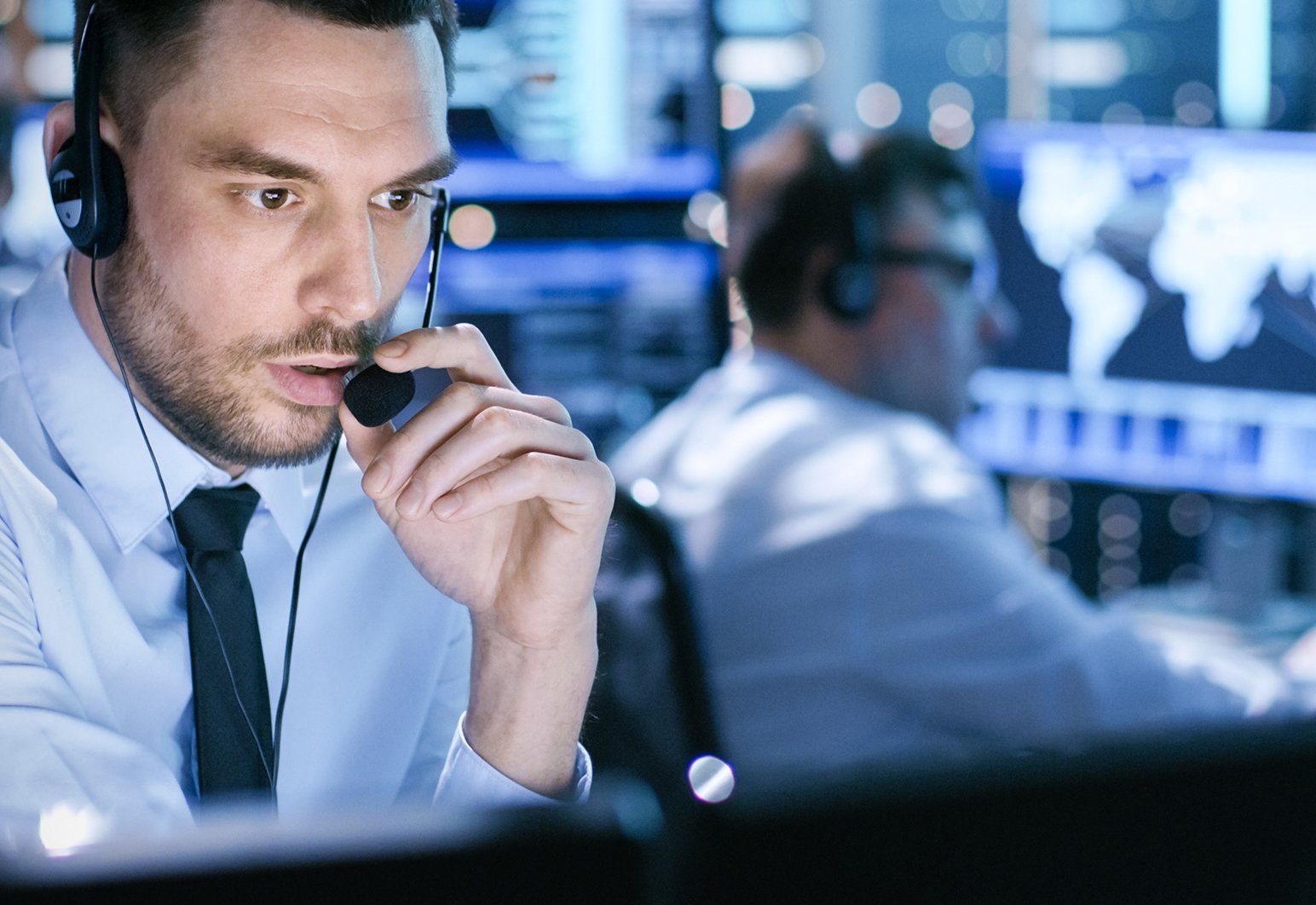 Man talking into head set looking at computer screens.
